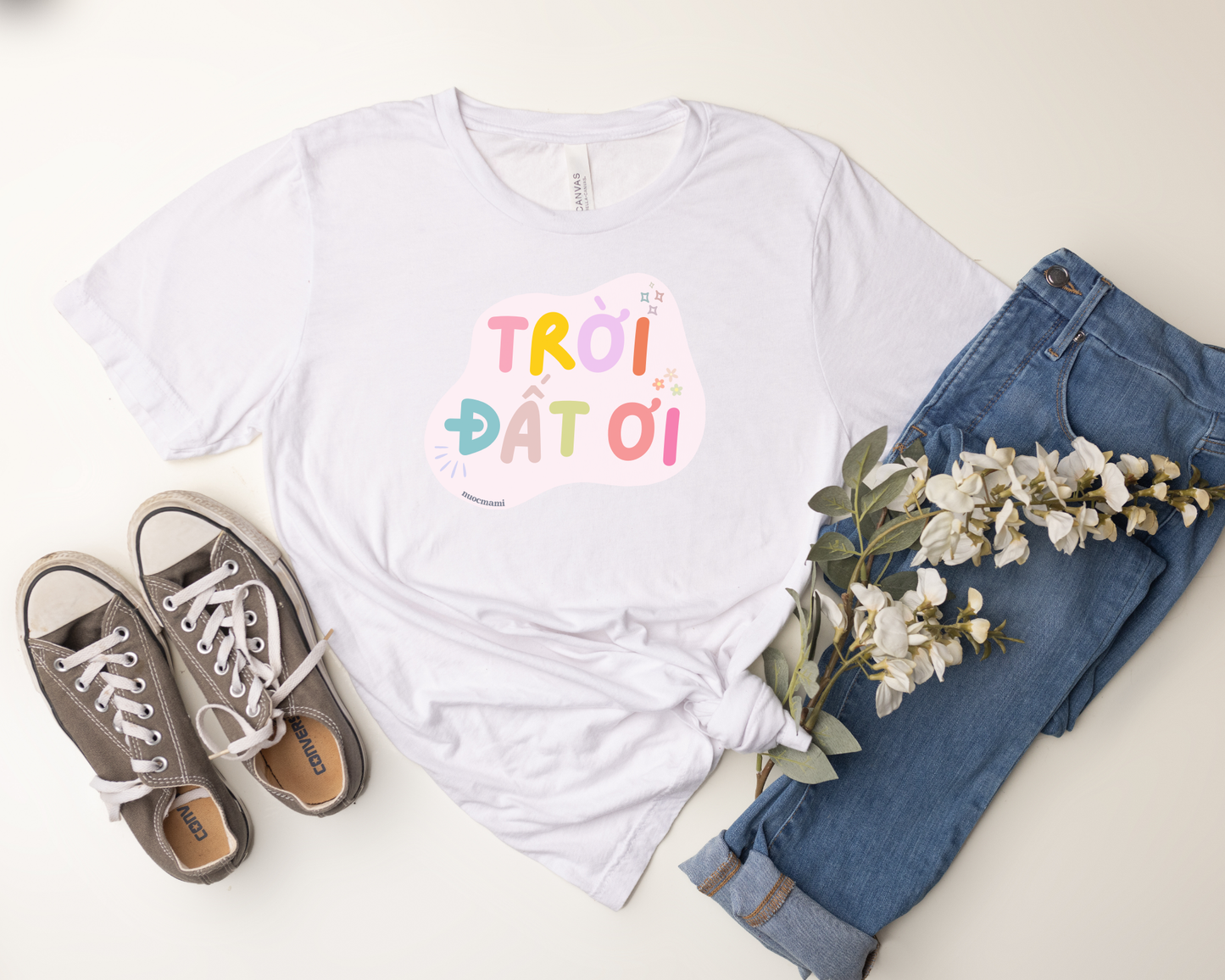 White t-shirt with colorful text, blue jeans, and brown sneakers on a light surface.