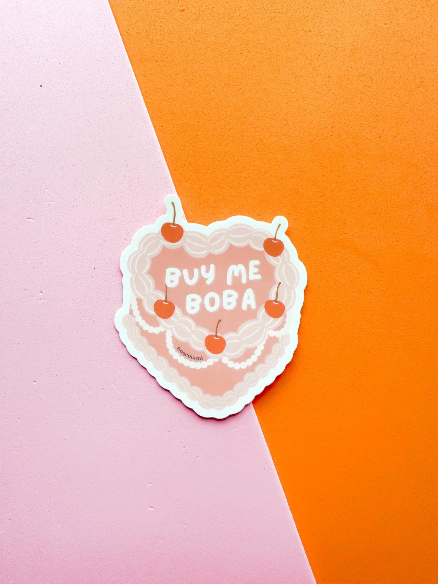 A matte premium vinyl sticker with the phrase 'BUY ME BOBA' written on a heart shaped cherry on top cake
