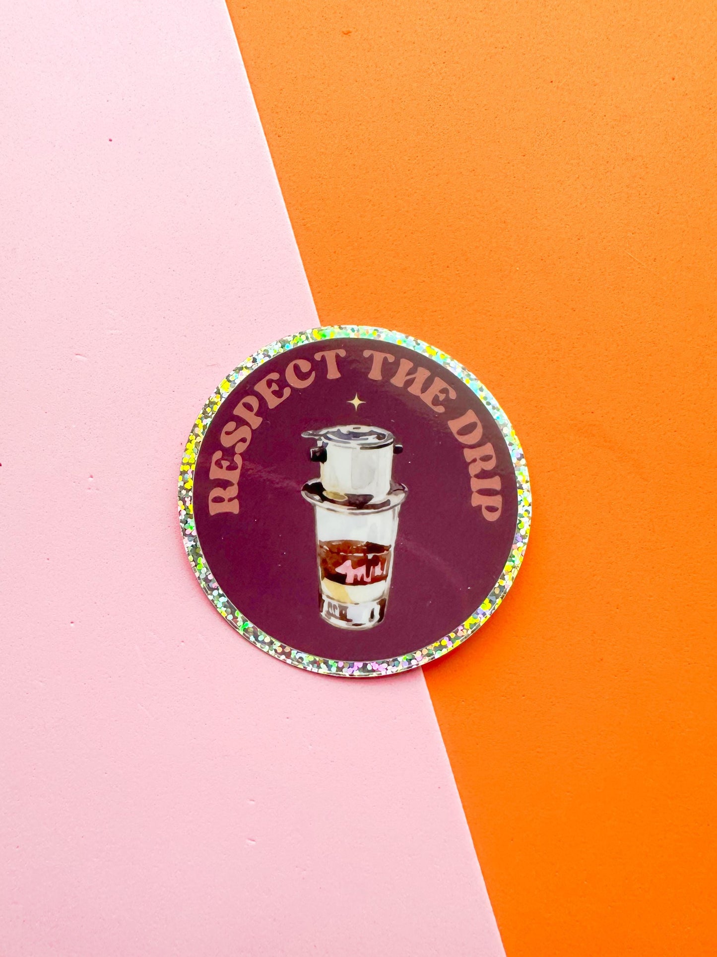 A round matte premium vinyl sticker with multicolored glitter text and a coffee cup illustration in the center, on  with the text 'Respect the Drip'.