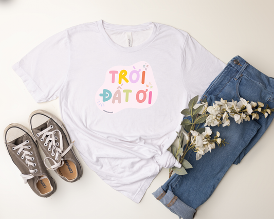 White t-shirt with colorful text, blue jeans, and brown sneakers on a light surface.