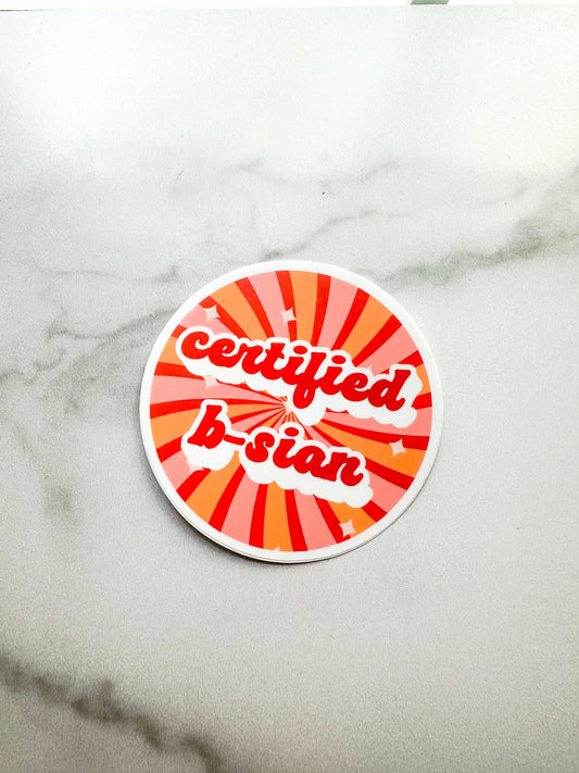 A round matte vinyl sticker with a red and orange background and the text 'certified b-sian' in red and white.