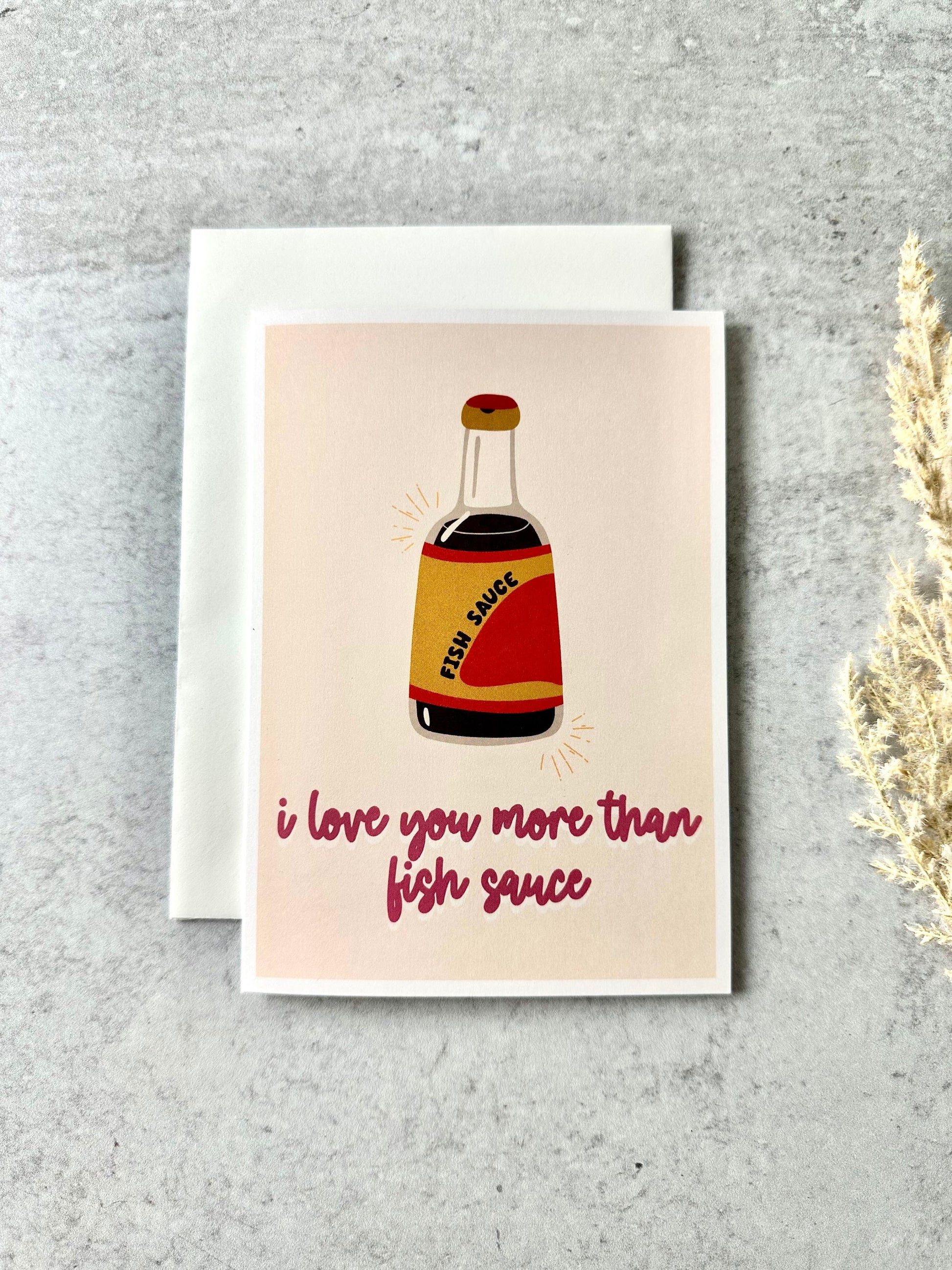 Greeting card with an illustration of a fish sauce bottle and the text 'i love you more than fish sauce' on a beige background.