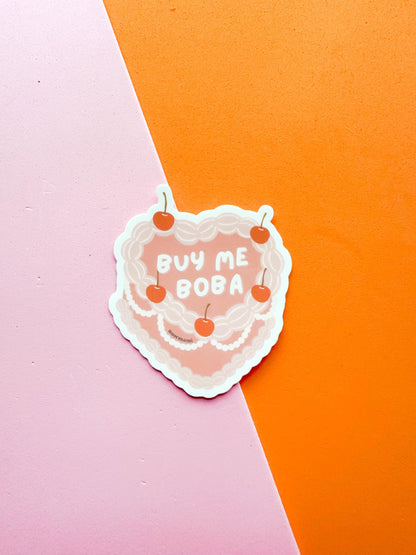 A matte premium vinyl sticker with the phrase 'BUY ME BOBA' written on a heart shaped cherry on top cake