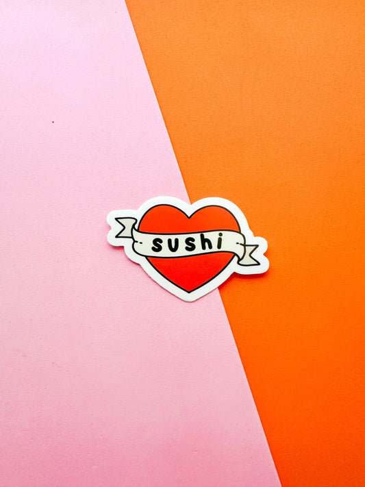A vinyl sticker with a red heart background, white banner with the word 'SUSHI' written in a stylized font 