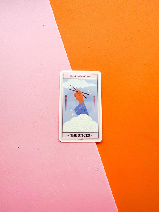 A vinyl sticker representing a tarot card titled 'The Sticks', featuring an illustration of a hand with chopsticks  with a clear blue sky and noodle like cloud in the background.