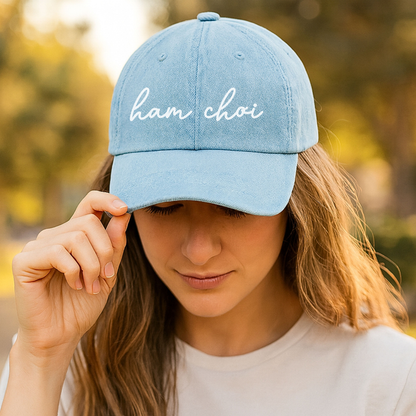 Person wearing a light blue cap with 'ham choi' text, outdoors.